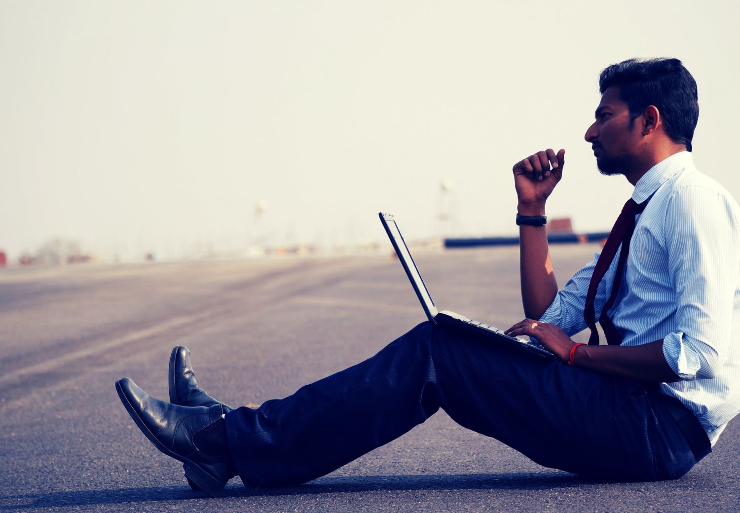  Ein Mann sitzt mit seinem Laptop auf einem asphaltierten Feld